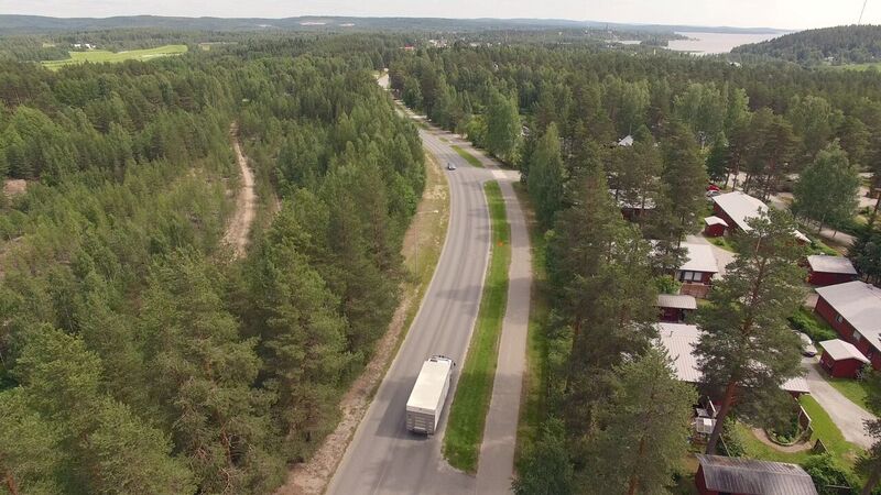 Puoliperävaunurekka ajaa maantiellä mäntymetsäisessa maisemassa, oikealla vieressä kevyenliikenteen väylä ja rivitaloasutusta 